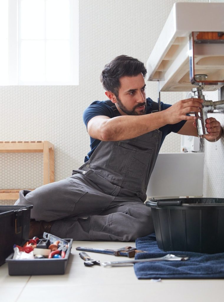 Male Plumber Working To Fix Leaking Sink In Home Bathroom
