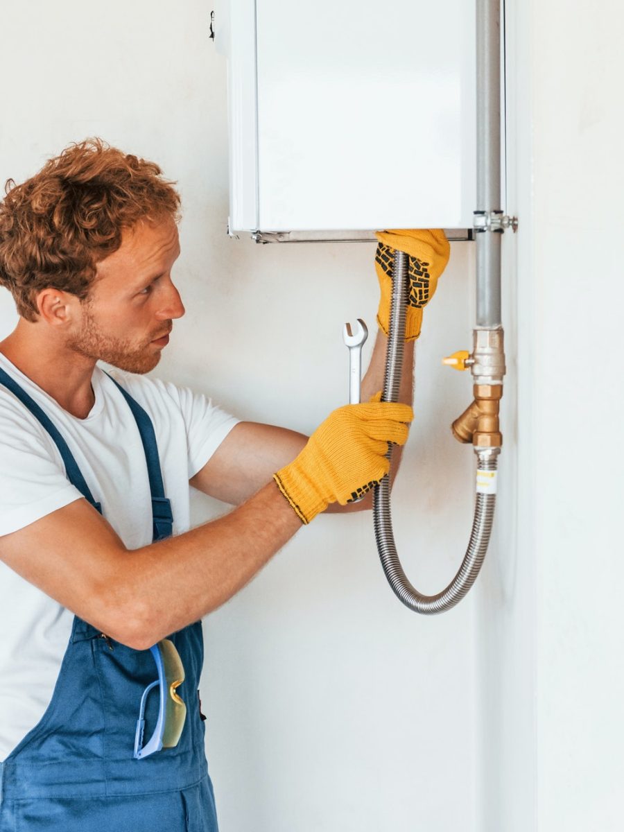 Repairing water heater. Young man working in uniform at construction at daytime